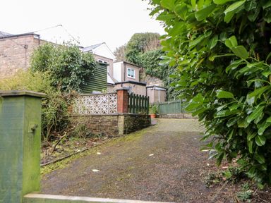 A driveway leading to a house with green wooden fences and dense greenery at Hunter Cottage in Haltwhistle near Hadrians Wall