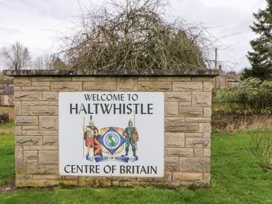 A welcome sign for Haltwhistle Centre of Britain on a stone wall surrounded by grass and trees