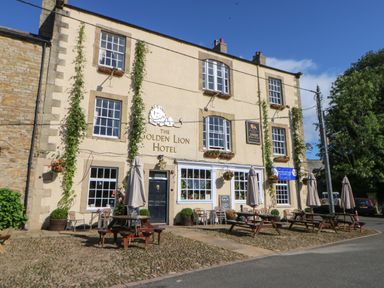 The exterior of The Golden Lion Hotel with outdoor tables and umbrellas on a cobblestone area at The Forge in Allendale