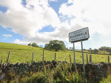A countryside scene with a welcome sign for Allendale next to a stone fence and grassy hills at The Forge in Allendale