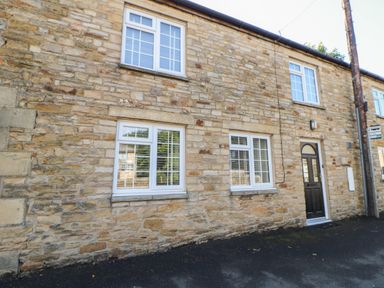 Stone exterior wall of a building with four white windows and a black door at The Forge in Allendale