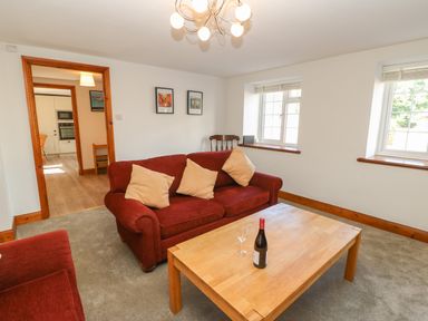 A living room with red sofas a wooden coffee table with a bottle and glass and two windows at The Forge in Allendale
