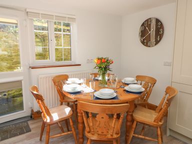 A dining area with a round wooden table set for six and a wall clock at The Forge in Allendale