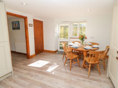 A dining area with a round wooden table set for six and wooden chairs next to a door and window at The Forge in Allendale