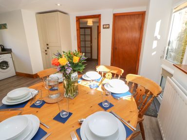 A dining table set with plates glasses and cutlery with a vase of flowers in a kitchen at The Forge in Allendale