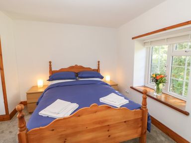 A bedroom with a wooden bed with blue bedding bedside tables with lamps and a window with flowers at The Forge in Allendale