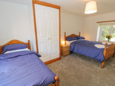 A bedroom with two wooden beds with blue bedding a bedside table a lamp white closet doors and a window with flowers on the sill at The Forge in Allendale
