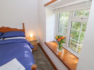 A bedroom with a wooden bed blue bedding a wooden nightstand with a lamp and flowers on a window sill at The Forge in Allendale