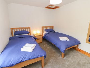 A bedroom with two single beds with blue bedding and folded white towels on a nightstand with lamps at The Forge in Allendale