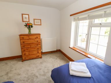 A bedroom with a wooden chest of drawers flowers on top a window with blinds and a bed with folded towels at The Forge in Allendale