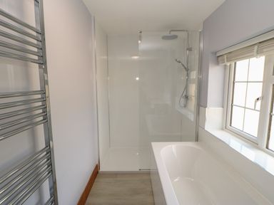 A bathroom with a bathtub a shower area with glass partition a window and a towel radiator at The Forge in Allendale