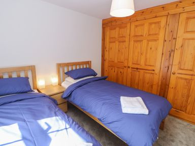 A bedroom with two single beds with blue bedding a wooden wardrobe and a bedside table with lamps at The Forge in Allendale