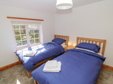 A bedroom with two single beds with blue bedding and white towels on them a small wooden nightstand with two lamps and a window with white blinds at The Forge in Allendale