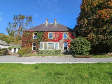A two-story house with ivy on the walls and a glass porch in front with trees and grass around at Carley's Bridge House in Carley's Bridge near Enniscorthy County Wexford