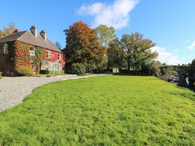 A house with ivy on the walls next to a gravel driveway and green lawn near trees and a river at Carley's Bridge House in Carley's Bridge near Enniscorthy County Wexford