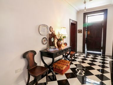 An entryway with black and white checkered floor two wooden chairs a black console table with books a lamp a clock and a basket on the floor at Carley's Bridge House Carley's Bridge near Enniscorthy County Wexford