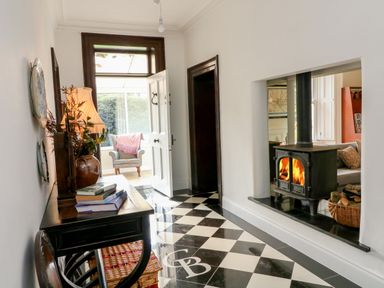 A hallway with a black and white checkered floor a wood stove with fire books on a table and a chair at Carley's Bridge House in Carley's Bridge near Enniscorthy County Wexford