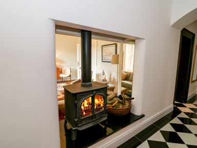 A wood burning stove with fire and a basket of logs next to it in a room with black and white tiled floor at Carley's Bridge House in Carley's Bridge near Enniscorthy County Wexford