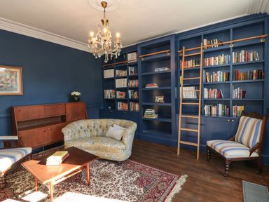 A sitting room with blue bookshelves a wooden ladder a patterned rug a wooden coffee table and assorted chairs at Carleys Bridge House in Carleys Bridge near Enniscorthy County Wexford