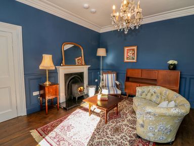 A living room with a fireplace a wooden coffee table a patterned rug a floral sofa a striped armchair a wooden cabinet and lamps at Carley's Bridge House in Carley's Bridge near Enniscorthy County Wexford