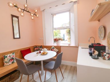 A dining area with a round white table gray chairs a wooden bench with cushions a coffee machine and a window at Carley's Bridge House Carley's Bridge near Enniscorthy County Wexford