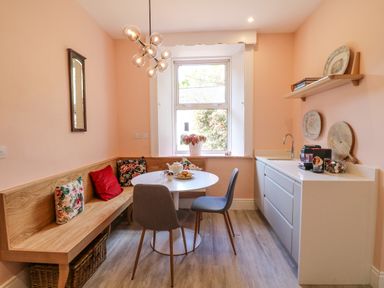 A dining area with a round white table two chairs a wooden bench with cushions and a kitchenette at Carleys Bridge House Carleys Bridge near Enniscorthy County Wexford