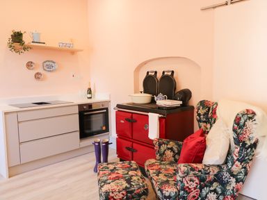 A kitchen with a beige cabinet and oven a red stove floral armchair and matching footstool at Carley's Bridge House in Carley's Bridge near Enniscorthy County Wexford
