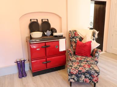 A red stove with a pot and teapot beside a floral-patterned armchair and ottoman with pillows at Carleys Bridge House Carleys Bridge near Enniscorthy County Wexford