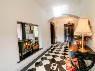 A hallway with a black and white checkered floor a fireplace with fire a wooden door and a table with a lamp and baskets at Carley's Bridge House in Carley's Bridge near Enniscorthy County Wexford