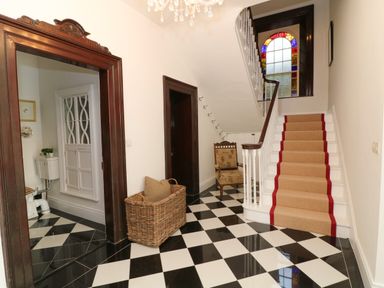 A hallway with black and white checkered floor a staircase with beige and red runner and a stained glass window at Carleys Bridge House in Carleys Bridge near Enniscorthy County Wexford