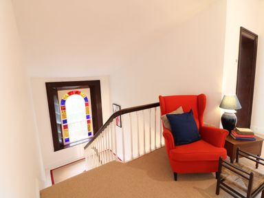 A landing area with a red armchair and cushions a side table with a lamp and books a small wooden chair and a stained glass window at Carleys Bridge House in Carleys Bridge near Enniscorthy County Wexford