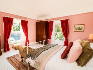 A bedroom with a bed chaise lounge red curtains a wooden wardrobe and a rug at Carleys Bridge House Carleys Bridge near Enniscorthy County Wexford