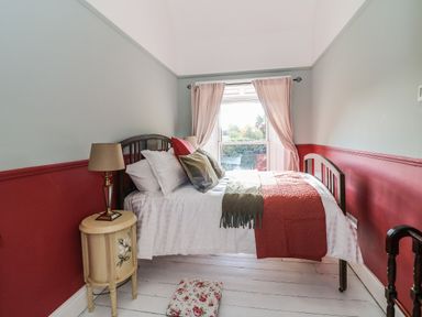 A bedroom with a bed pillows lampshade bedside table and window with curtains at Carley's Bridge House in Carley's Bridge near Enniscorthy County Wexford