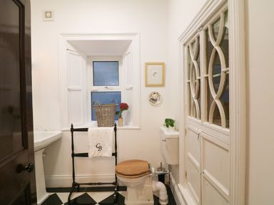 A bathroom with a toilet a wooden seat a towel rack with a towel a pedestal sink a window with a basket and flower a cabinet with glass doors at Carley's Bridge House in Carley's Bridge near Enniscorthy County Wexford