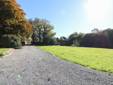 A gravel driveway beside a grass lawn with trees and a stone bridge in the background at Carley's Bridge House in Carley's Bridge near Enniscorthy County Wexford