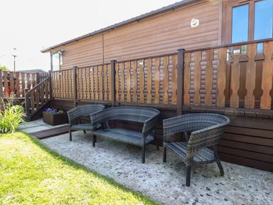 A patio area with outdoor wicker chairs and bench next to a wooden cabin at Doormouse Lodge South Lakeland Leisure Village