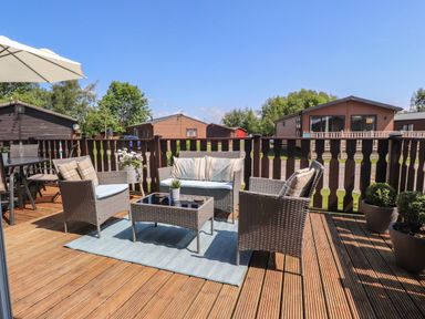 An outdoor deck with wicker chairs a table an umbrella and potted plants at Doormouse Lodge in South Lakeland Leisure Village
