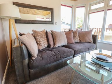 A living room with a dark sofa with multiple pillows a standing lamp a rectangular mirror and a glass coffee table with a tray and remote controls at Doormouse Lodge South Lakeland Leisure Village