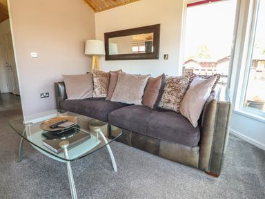 A living room with a sofa and pillows beside a glass coffee table at Doormouse Lodge in South Lakeland Leisure Village