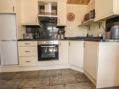 A kitchen with cream cabinets black countertops and tiled floor at Doormouse Lodge South Lakeland Leisure Village