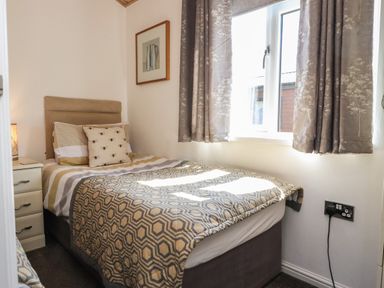 A small bedroom with a single bed patterned bedding bedside table and window with curtains at Doormouse Lodge South Lakeland Leisure Village