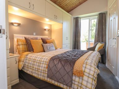 A bedroom with a double bed yellow and gray bedding built in cupboards and a window with gray curtains at Doormouse Lodge South Lakeland Leisure Village