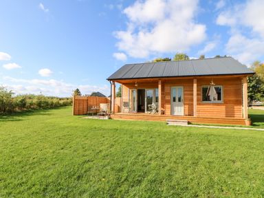 A wooden cabin with a porch and outdoor seating on a grassy lawn at Rising Sun in Kirkbymoorside