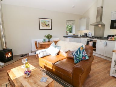 A living room with a leather sofa and wooden coffee table and a kitchen with white cabinets and a stove at Rising Sun in Kirkbymoorside