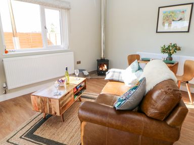 A living room with a brown leather sofa and wooden coffee table near a window and stove at Rising Sun in Kirkbymoorside