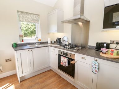 A kitchen with white cabinets a gas stove an oven a sink under a window and a countertop with small appliances and items at Rising Sun in Kirkbymoorside