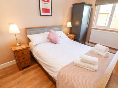 A bedroom with a double bed white linens pink pillow and folded towels on a pink blanket two wooden nightstands with lamps a gray wardrobe and a window at Rising Sun in Kirkbymoorside