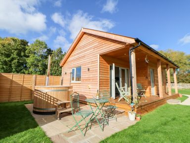 A wooden cabin with a hot tub and outdoor table and chairs on a patio at Rising Sun in Kirkbymoorside