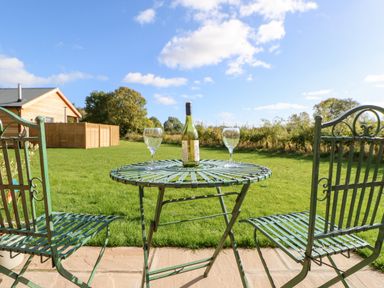 An outdoor metal table with a bottle and two wine glasses on a stone patio with two metal chairs and a grassy yard at Rising Sun in Kirkbymoorside