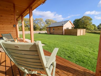 A wooden porch with chairs overlooking a grassy yard and a small wooden cabin at Rising Sun in Kirkbymoorside